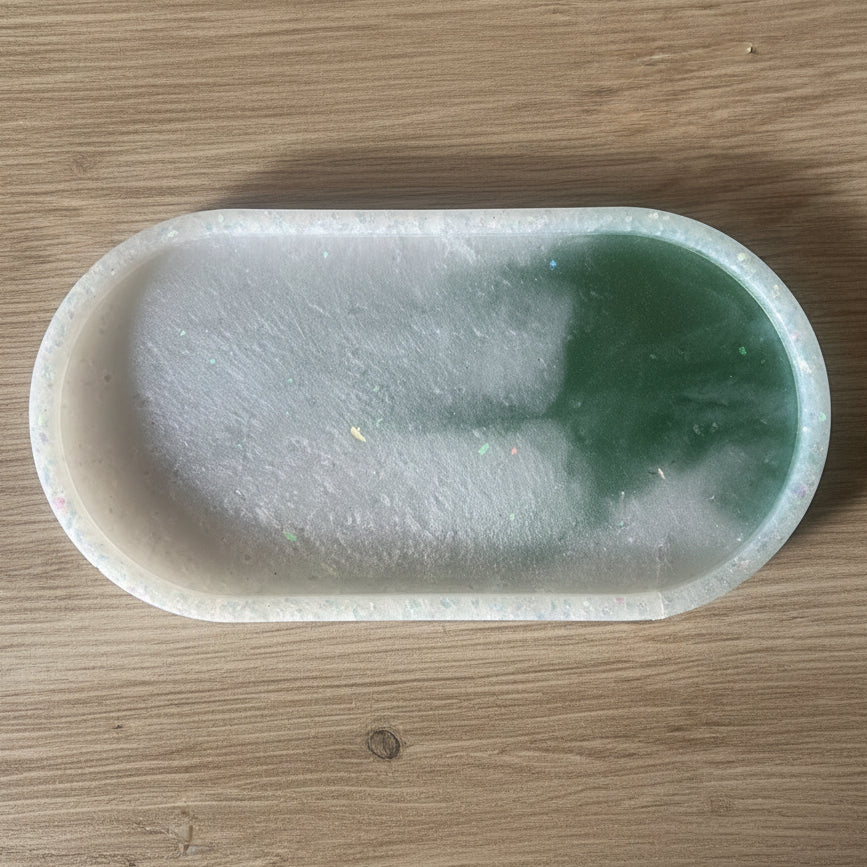 An oval-shaped translucent jadeite jewelry mold or tray with a green and white color gradient, resting on a light brown wooden surface.
