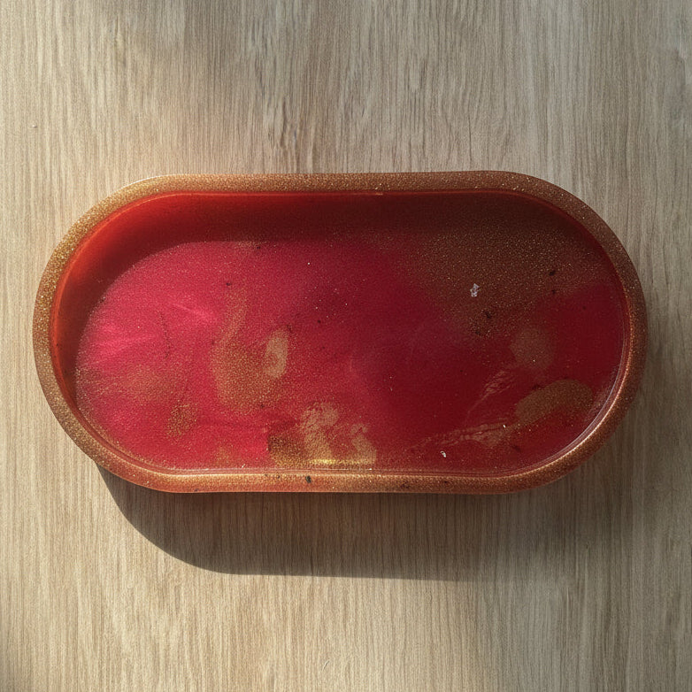 An oval-shaped wooden tray with a glossy red and gold glitter finish, placed on a light wood grain surface.